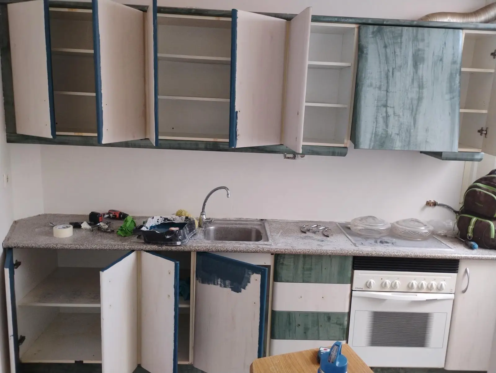Trabajos de pintura en muebles de cocina con puertas abiertas y herramientas de lacado en Alicante