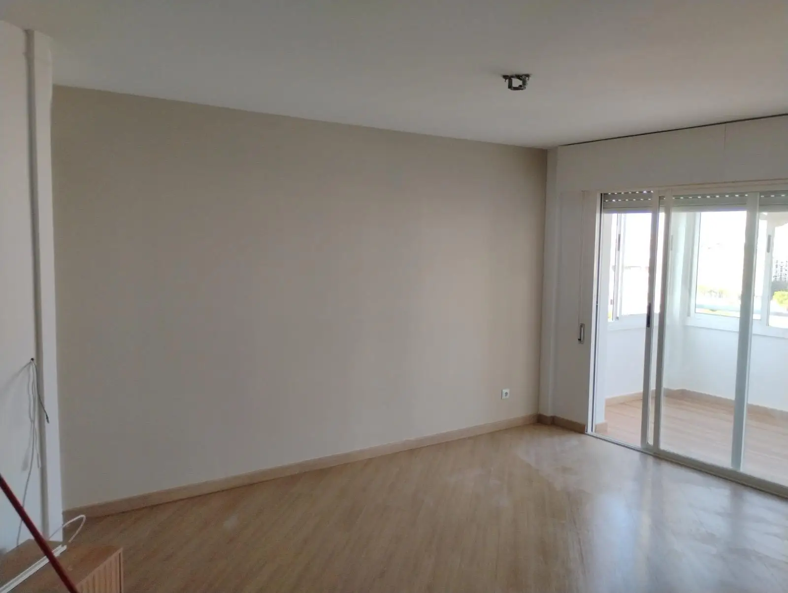 Servicio de pintura en salón con pared beige, suelo de tarima y ventanal en Alicante